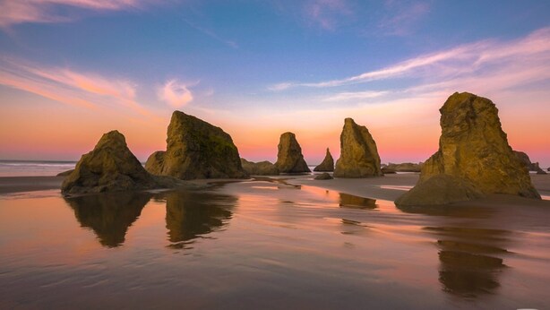 Ein Strand mit großen Felsformationen und ruhigem Wasser, das den Sonnenuntergang spiegelt.