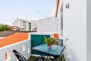 Un petit balcon extérieur avec une table, un pot de fleurs et une porte à volets verts.