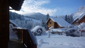 Une cabane en bois avec une terrasse enneigée et une vue sur les montagnes en arrière-plan.
