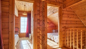 Une chambre située dans une cabane en rondins, avec un plafond en bois, une fenêtre avec des rideaux, un lit et une petite table.