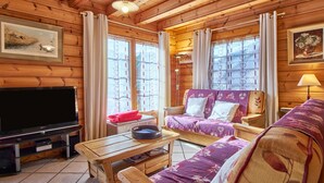 L'intérieur d'un chalet en bois, avec un canapé, un téléviseur et une table à manger.