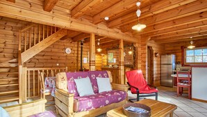L’intérieur d’une cabane en rondins, avec un escalier en bois, un canapé, une table à manger et un coin cuisine.