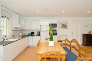 A modern kitchen with white cabinets, a wooden dining table with blue cushions, and a potted plant.