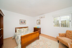 A bedroom with a wooden bed, a nightstand, a chair, and a window with a view.