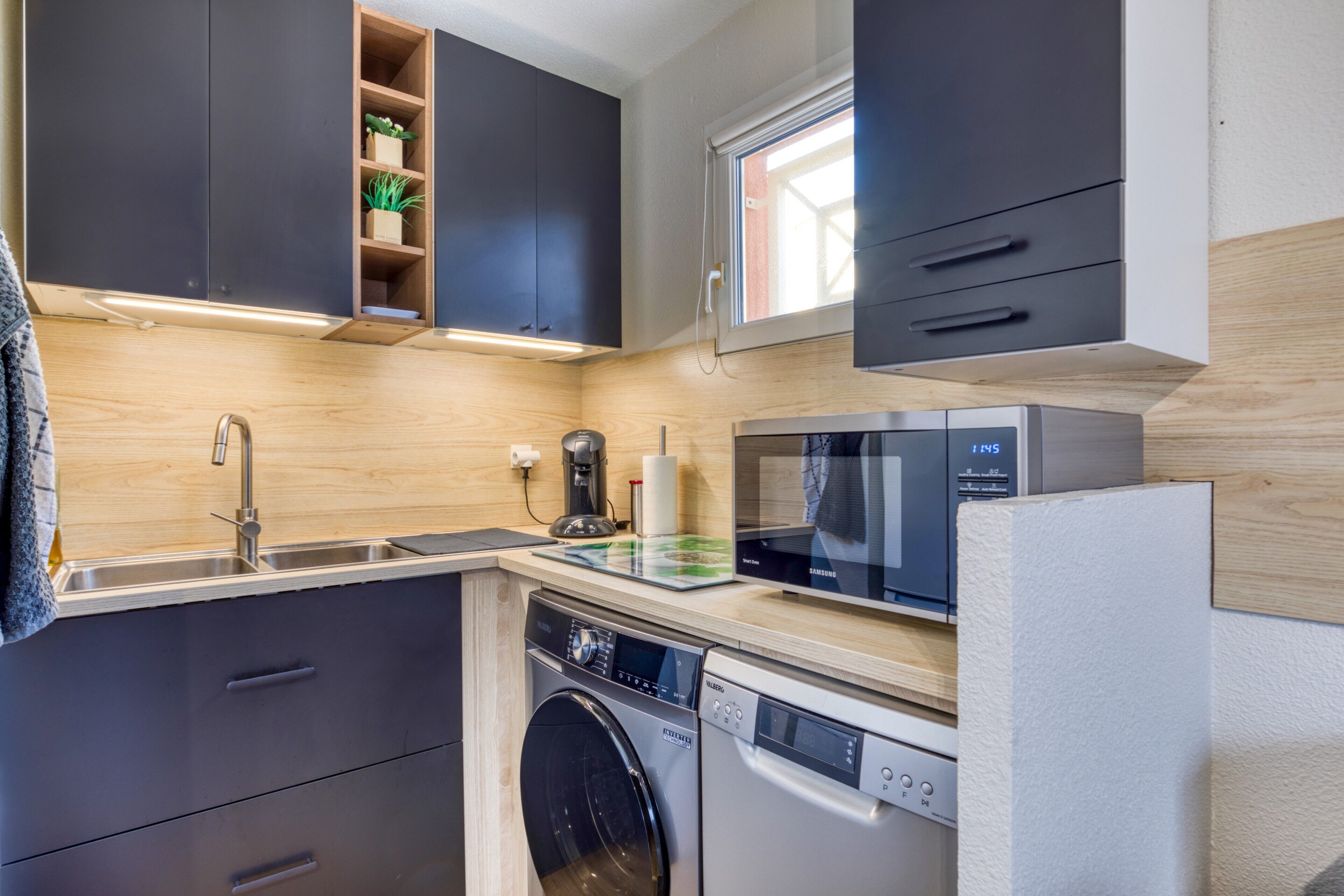 Une cuisine compacte équipée d’un lave-linge, d’un four à micro-ondes et d’une fenêtre située au-dessus de l’évier.