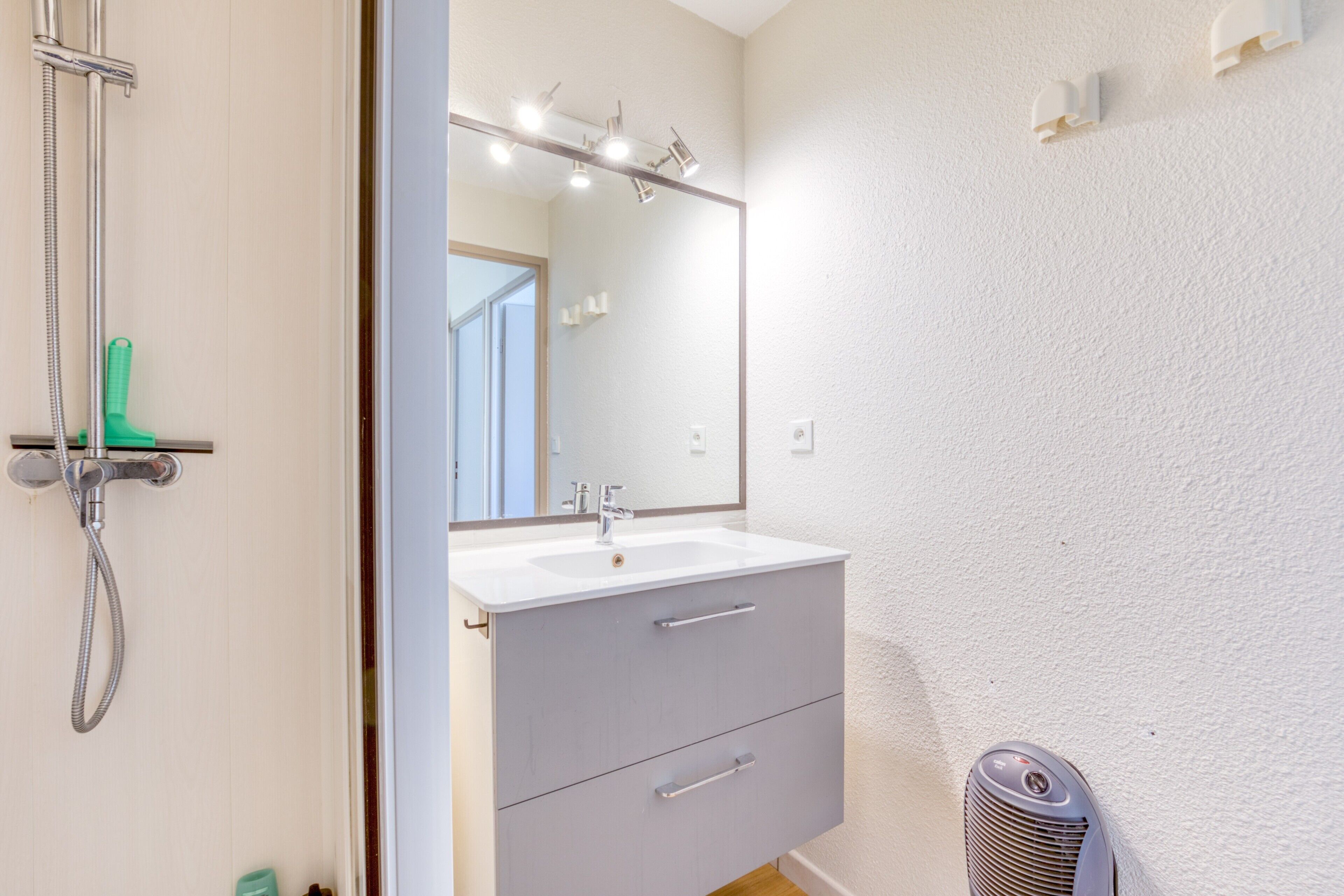A bathroom with a white sink, a mirror, a shower, and a ventilation unit.