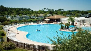 A large, curved swimming pool surrounded by lounge chairs and a wooden fence.