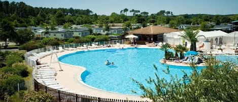 Ein großer, bogenförmiger Pool, umgeben von Liegestühlen und einem Holzzaun.