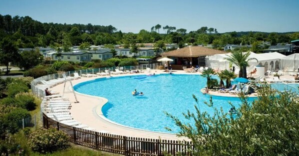 A large, curved swimming pool surrounded by lounge chairs and a wooden fence.