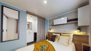 A modern bedroom with a bed, bedside tables, a mirror, and a built-in wardrobe.