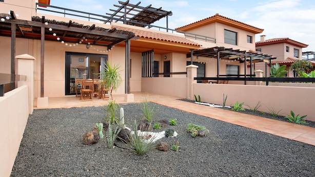 Une maison moderne dotée d’un patio, d’un espace salon extérieur et d’un jardin planté de cactus.