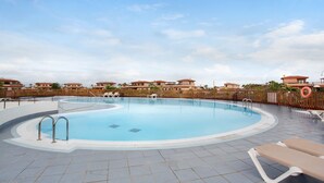 Une piscine avec une terrasse carrelée, des chaises longues et une clôture en bois.