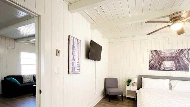 A bedroom with a bed, a chair, a nightstand, a TV, and a wall with a framed picture. - Cozy one bedroom across from the beach #2 (North Myrtle Beach)