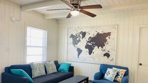 A room with a dark blue sofa, a matching armchair, and a small table. A world map mural is on the wall, and there's a ceiling fan. - Cozy one bedroom across from the beach #2 (North Myrtle Beach)