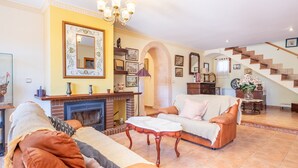 Un salon avec une cheminée, un escalier et un lustre.