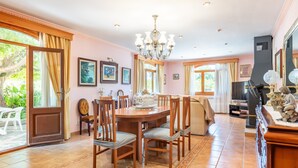 Un coin repas avec une table en bois, des chaises et un lustre. Les murs sont ornés de tableaux encadrés, et on y trouve également un téléviseur et une cheminée.
