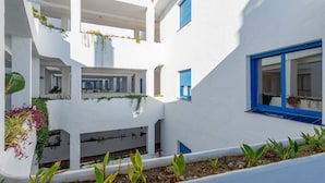 Un bâtiment blanc avec des encadrements de fenêtres bleus, des balcons ornés de plantes et une cour intérieure.