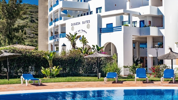 Un hôtel doté d’une piscine, de chaises longues et d’une enseigne indiquant « DUQUESA SUITES ».