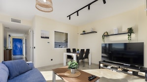 Un salon comprenant un canapé, une table basse avec une plante, un téléviseur et un coin repas avec des chaises et une table.
