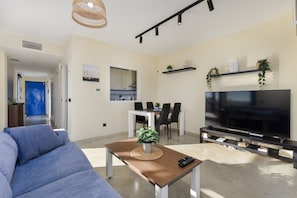 Una sala de estar con sofá, mesa de centro con planta, televisor y comedor con sillas y mesa.