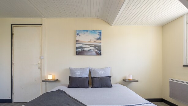 A bedroom with a bed, pillows, a painting, bedside lamps, and a door.