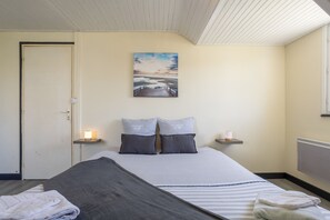 Quarto com cama, almofadas, um quadro, abajures e uma porta.