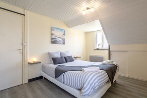 A bedroom with a bed, bedside tables, a wall-mounted light, a painting, and a window.
