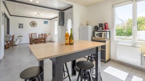 A modern kitchen with a wooden table, bar stools, a refrigerator, a microwave, and a large window.