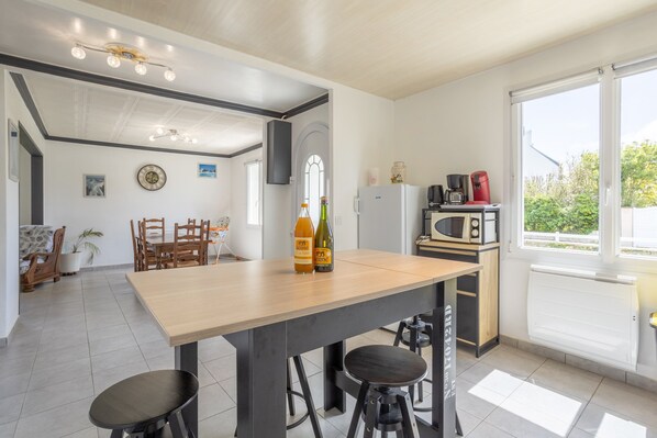 A modern kitchen with a wooden table, bar stools, a refrigerator, a microwave, and a large window.