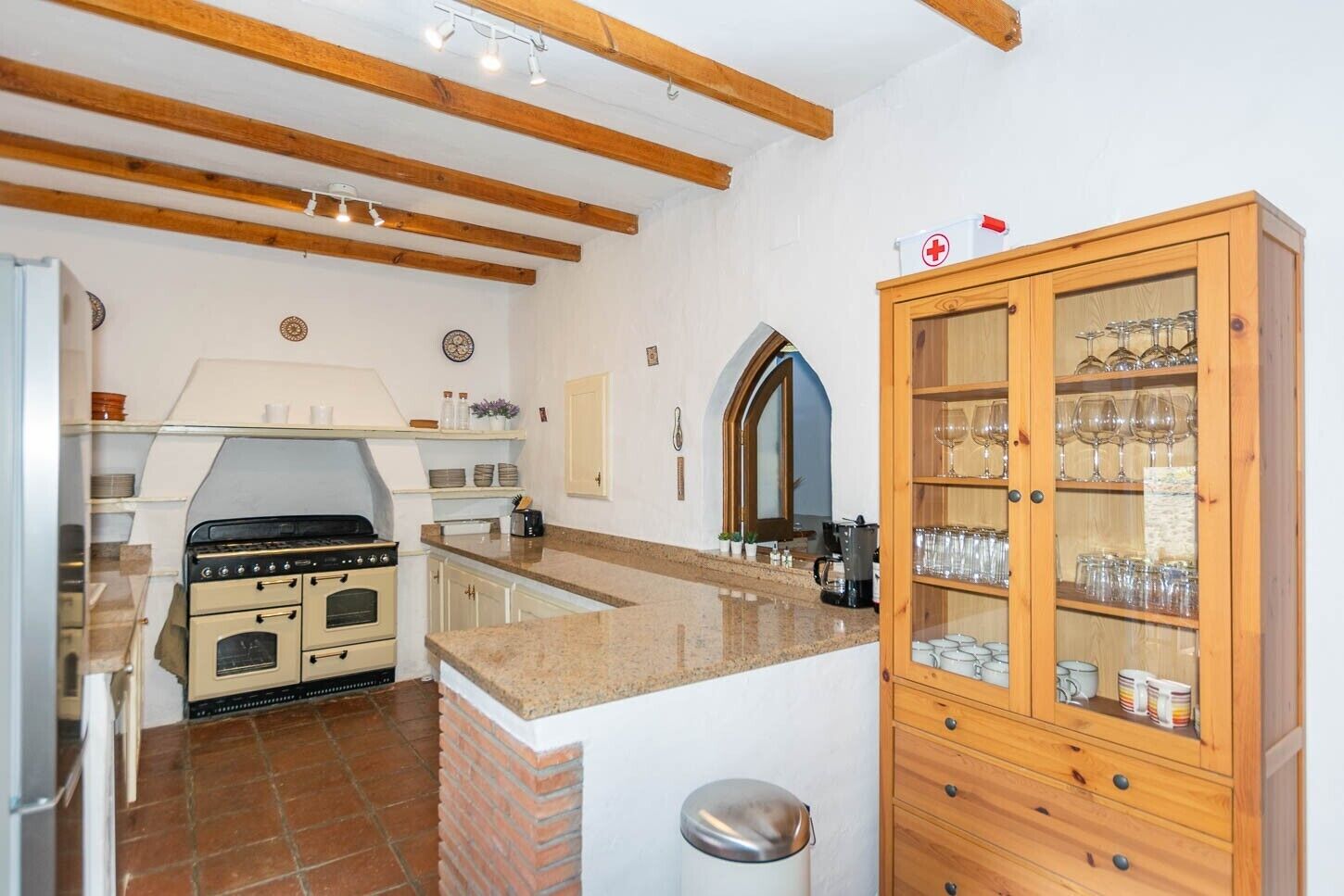 A kitchen with a stove, oven, and a cabinet with glassware.