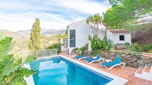 Eine moderne Villa mit Swimmingpool, Liegestühlen und Blick auf die umliegende Landschaft.