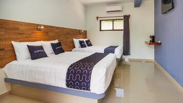 A hotel room with two beds, a wooden headboard, an air conditioning unit, a small shelf, and a window with curtains.