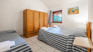 Une chambre avec deux lits, une armoire en bois, un tableau et une fenêtre avec des rideaux.