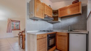 A compact kitchen with wooden cabinets, a built-in oven, a refrigerator, and a window with curtains.