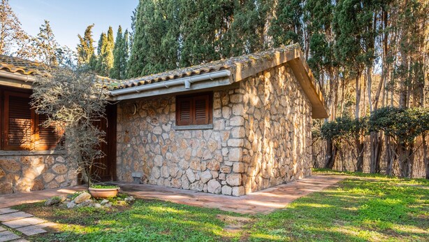 A stone building with a tiled roof, a window with shutters, and a pathway leading to it.