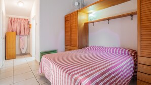 A bedroom with a bed, wooden wardrobe, and a fan.