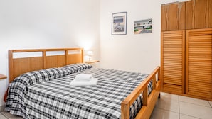 Un dormitorio con cabecera de cama de madera, colcha a cuadros, lámpara de noche y armario de madera.