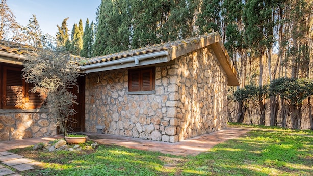 Un edificio de piedra con techo de tejas, una ventana con contraventanas y un sendero que lo lleva a él.