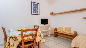 A small room with a dining table, chairs, a TV, a bench, and a shelf. - ‘La Capannuccia D’ Apartment with Shared Garden, Wi-Fi, and Air Conditioning (Ansedonia)
