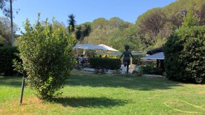 A grassy outdoor area with a statue, a covered structure, and trees in the background. - ‘La Capannuccia D’ Apartment with Shared Garden, Wi-Fi, and Air Conditioning (Ansedonia)