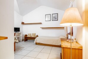 Quarto com cama, escrivaninha, televisão e luminária.