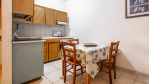 A compact kitchen with wooden cabinets, a dining table with chairs, and a tiled floor. - ‘La Capannuccia D’ Apartment with Shared Garden, Wi-Fi, and Air Conditioning (Ansedonia)