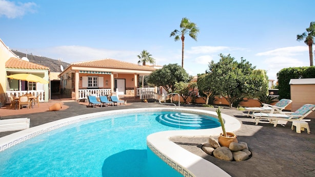 A swimming pool with lounge chairs, a small garden, and a building with a tiled roof. - Eveas – Private Villa with Pool in Tenerife (Candelaria)