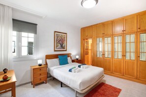 A bedroom with a bed, bedside tables, a nightstand, a window, a painting, and wooden wardrobe doors. - Eveas – Private Villa with Pool in Tenerife (Candelaria)