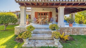 A covered patio with a stone staircase leading to a wooden door, surrounded by potted plants and a grassy lawn. - Villa 'Ginebro Puerto Pollença' with Private Pool, Wi-Fi and Air Conditioning (Puerto Pollença)