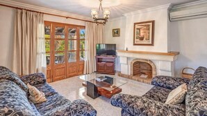 A living room with a fireplace, a television, and patterned sofas. - Villa 'Ginebro Puerto Pollença' with Private Pool, Wi-Fi and Air Conditioning (Puerto Pollença)