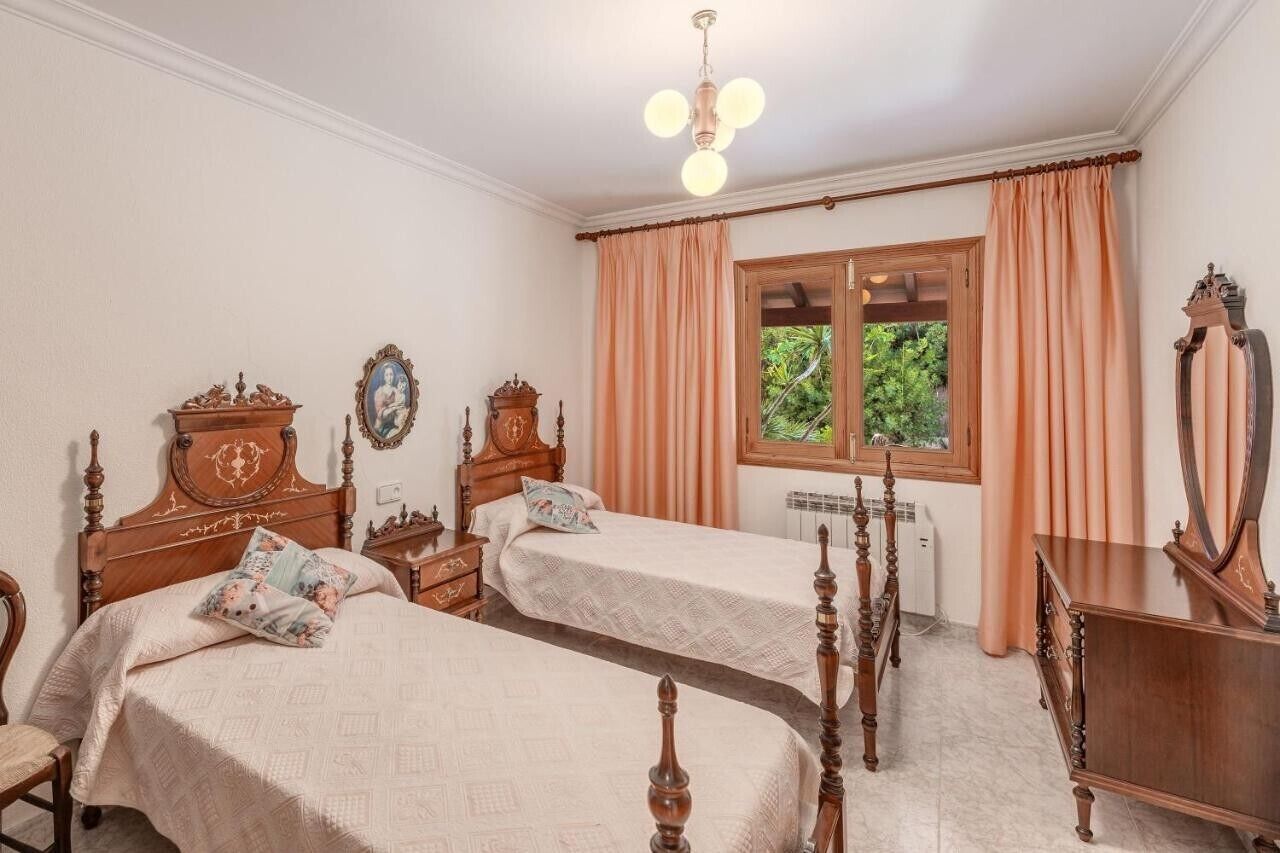 A room with two wooden beds, a wooden dresser, a mirror, and a window with curtains.