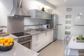 A modern kitchen with white cabinetry, a stainless steel range hood, a microwave, and a refrigerator.