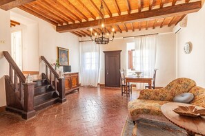 A spacious living area with a wooden staircase, a floral sofa, and a dining table. - Vacation Home "Residenza D'Epoca Alcova" with Shared Pool, Shared Garden & Wi-Fi (lucignano)