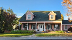 A two-story house with a front porch, a chimney, and a garage. - Alegria!  Five Bedroom Colonial Style Home Conveniently Located! Pet Friendly! (Moses Lake)